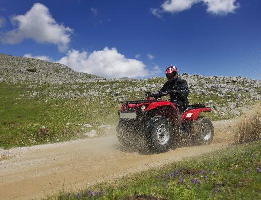 Pilote en quad traversant un chemin tout-terrain en pleine nature, projetant de l’eau et de la poussière.