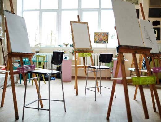 Atelier de peinture avec plusieurs chevalets, feuilles blanches et tabourets dans une salle lumineuse.