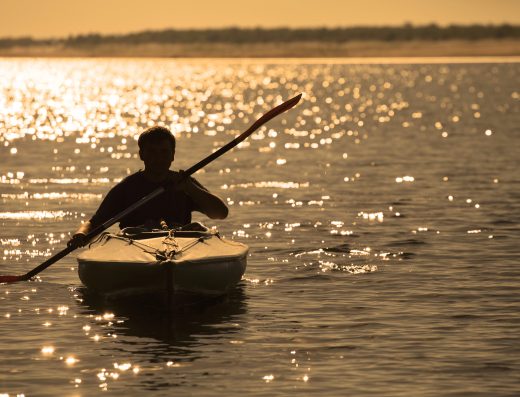 Personne pratiquant le kayak sur un plan d’eau au coucher du soleil
