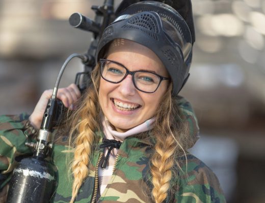 Jeune femme souriante en tenue camouflage tenant un lanceur de paintball