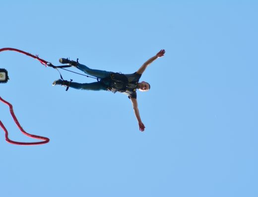 Personne en plein saut à l’élastique, attachée par les pieds, bras écartés dans le ciel.