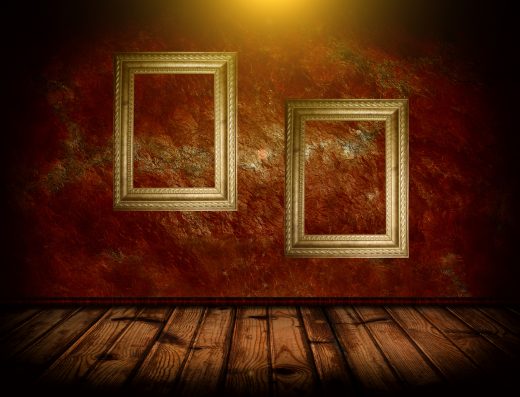 Deux cadres dorés vides accrochés sur un mur rouge texturé, avec un sol en bois sombre.