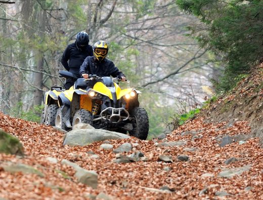 Deux personnes en randonnée en quad traversant un chemin forestier rocailleux.