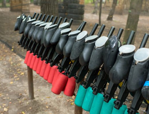 Ligne de lanceurs de paintball alignés sur un râtelier dans un terrain extérieur boisé.