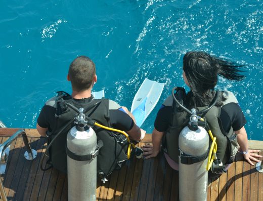 Couple équipé pour une plongée sous-marine prêt à entrer dans une eau turquoise depuis un bateau.