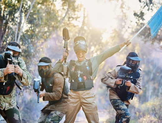 Équipe de joueurs de paintball en action, dont un portant un drapeau bleu en signe de victoire