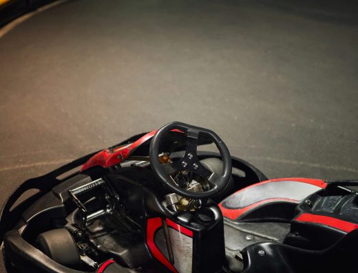Kart de course rouge et noir stationné sur une piste de karting indoor.