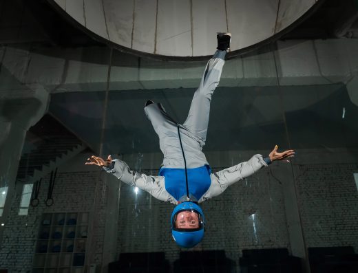 Personne en chute libre indoor dans un simulateur de vol, équipée d’une combinaison et d’un casque.
