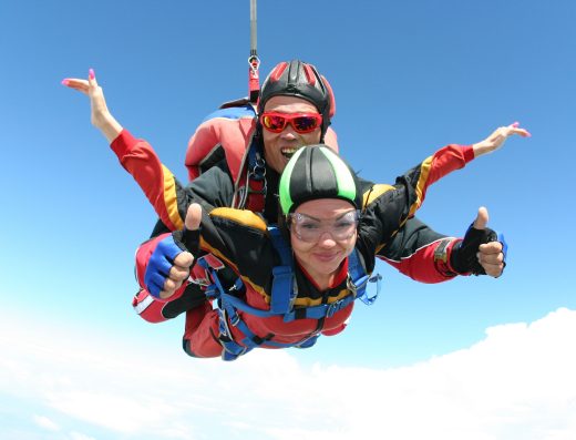 Deux personnes effectuant un saut en parachute en tandem, en chute libre sous un ciel bleu.
