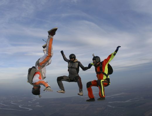 Trois personnes en chute libre lors d’un saut en parachute, formant une figure en plein ciel.